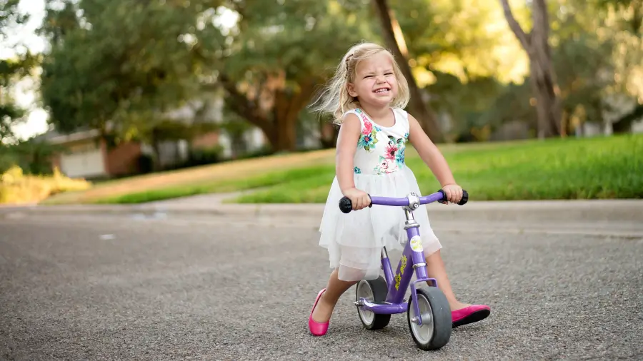 Mädchen sitzt auf ihrem Laufrad und lacht fröhlich